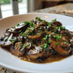Close-up of sliced mushrooms coated in a rich brown mushroom sauce and garnished with fresh parsley.
