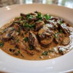 Close-up of a rich mushroom sauce, featuring sliced mushrooms coated in a creamy brown sauce and topped with fresh parsley.