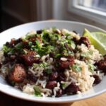 Close-up of a bowl of savory 1-pot black beans and rice topped with seasoned sausage chunks and fresh cilantro.
