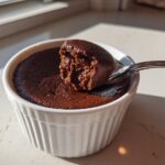 A spoonful of rich, dark chocolate mousse being lifted from a white ramekin.