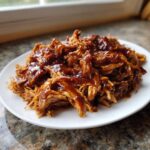 A plate piled high with shredded crockpot teriyaki chicken coated in a thick, glossy teriyaki sauce.