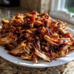 A mound of shredded crockpot teriyaki chicken heavily coated in glossy teriyaki sauce, served on a white plate.