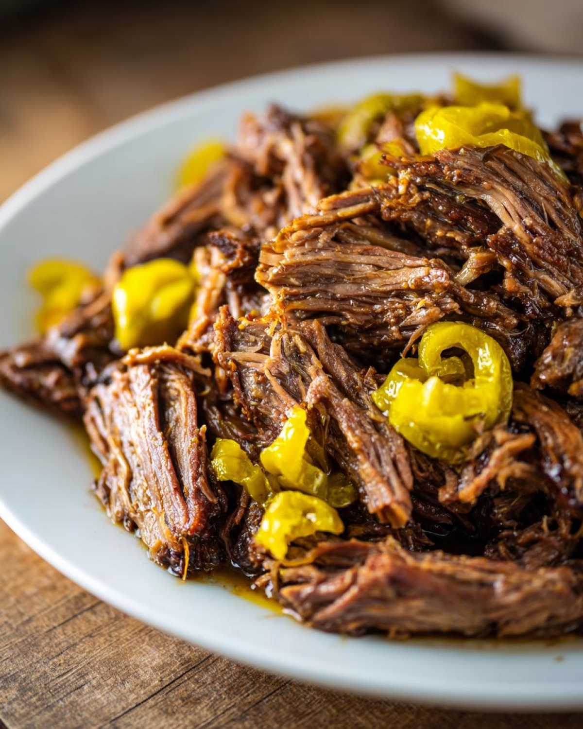 Close-up of shredded Mississippi pot roast served on a white plate, topped with bright yellow pepperoncini slices.