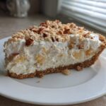 A thick slice of million dollar pie featuring a graham cracker crust, creamy filling with pineapple chunks, and a pecan topping.