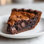 A close-up of a decadent slice of fudge pie showing a gooey, dark chocolate interior and visible chocolate chips.
