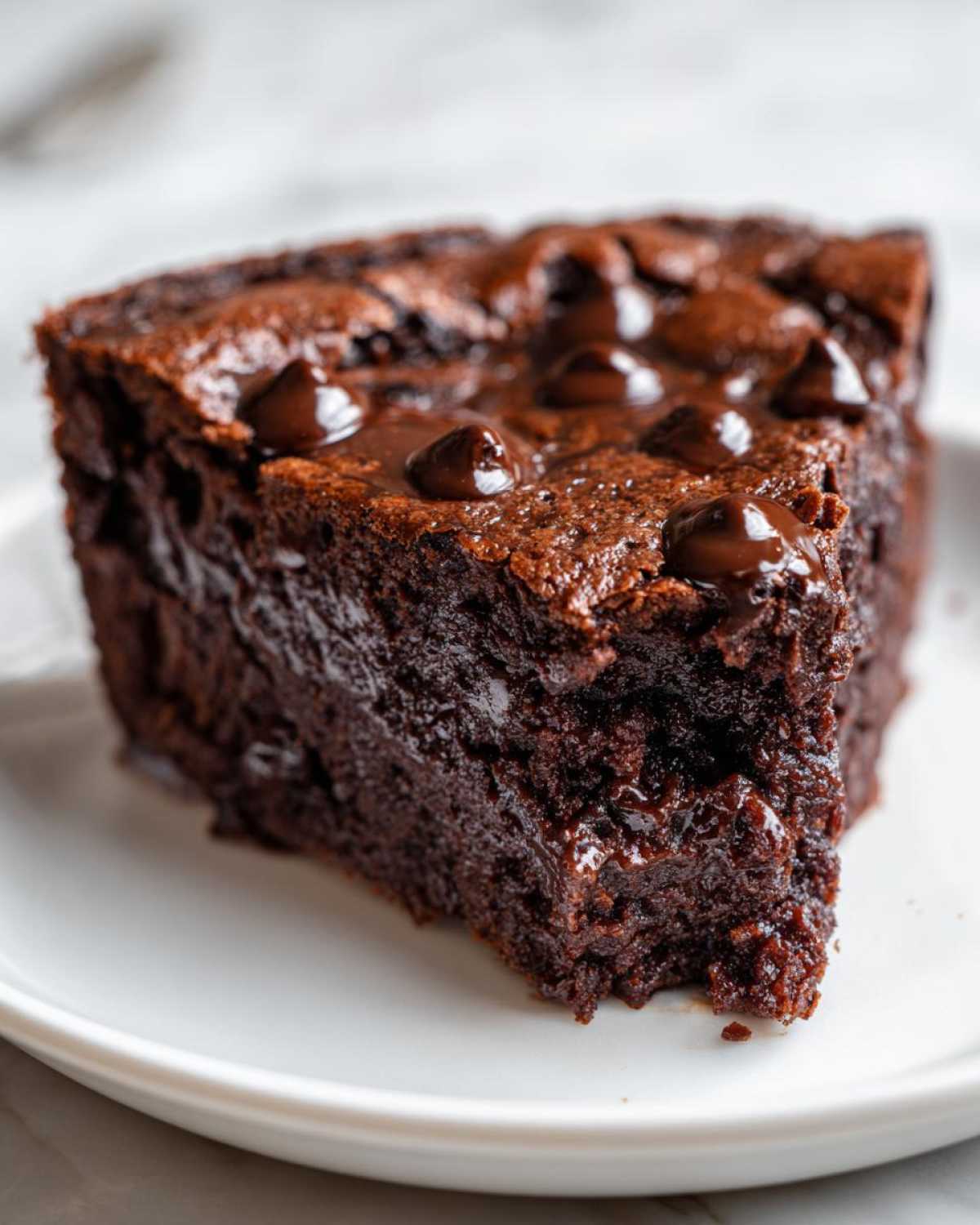 Close-up of a decadent slice of fudge pie on a white plate, featuring a moist, dark chocolate interior and melted chocolate chips.