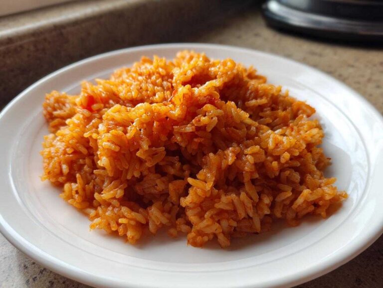 Close-up of vibrant, reddish-orange Smoky jollof rice piled high on a white plate.