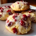 Four soft cranberry orange cookies topped with a white glaze and dried cranberries, sitting on a white plate.