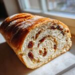 Close-up of a freshly baked soft raisin bread loaf, showing the swirl pattern and plump raisins inside.