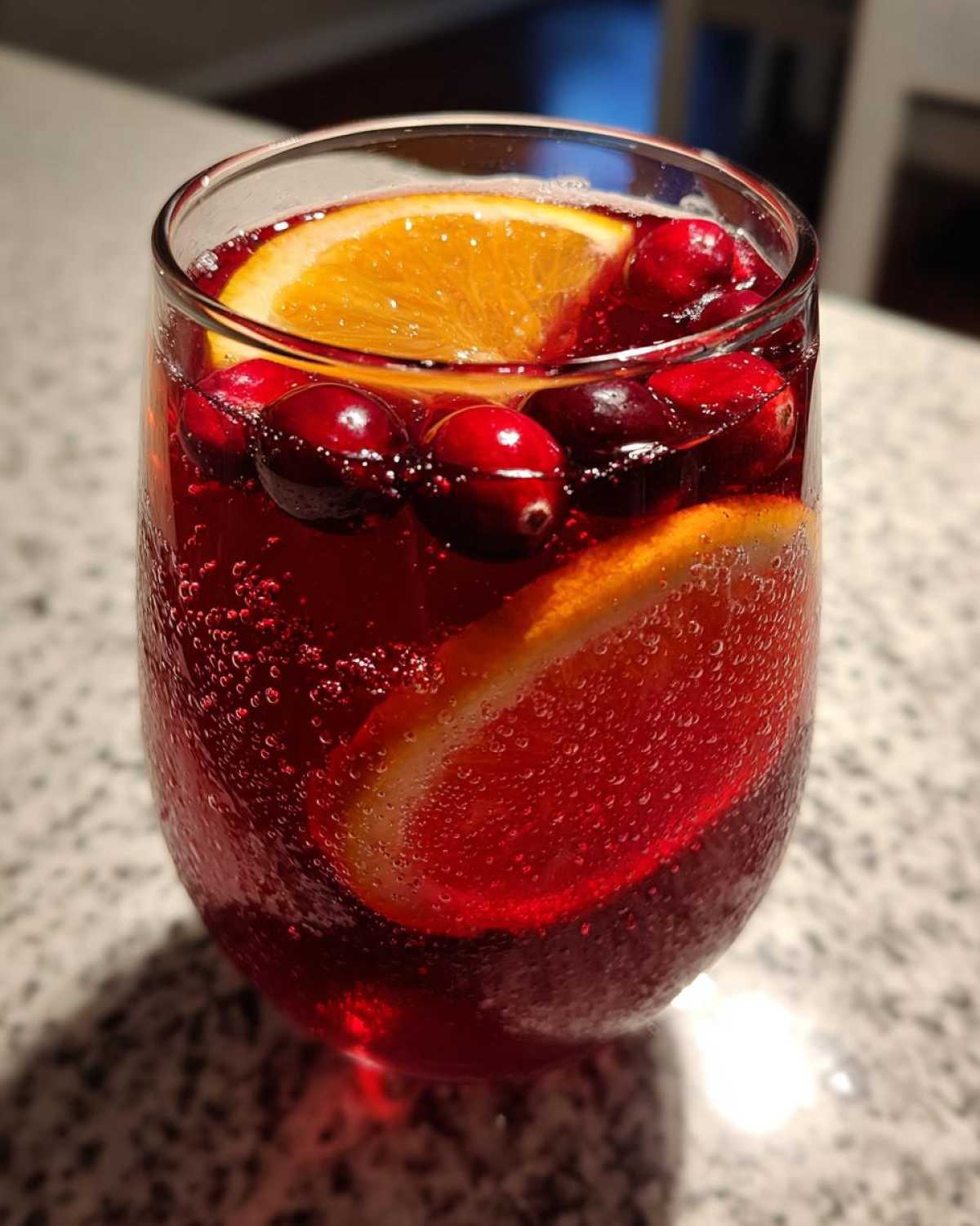 A close-up of a glass filled with sparkling red thanksgiving punch, garnished with fresh cranberries and orange slices.