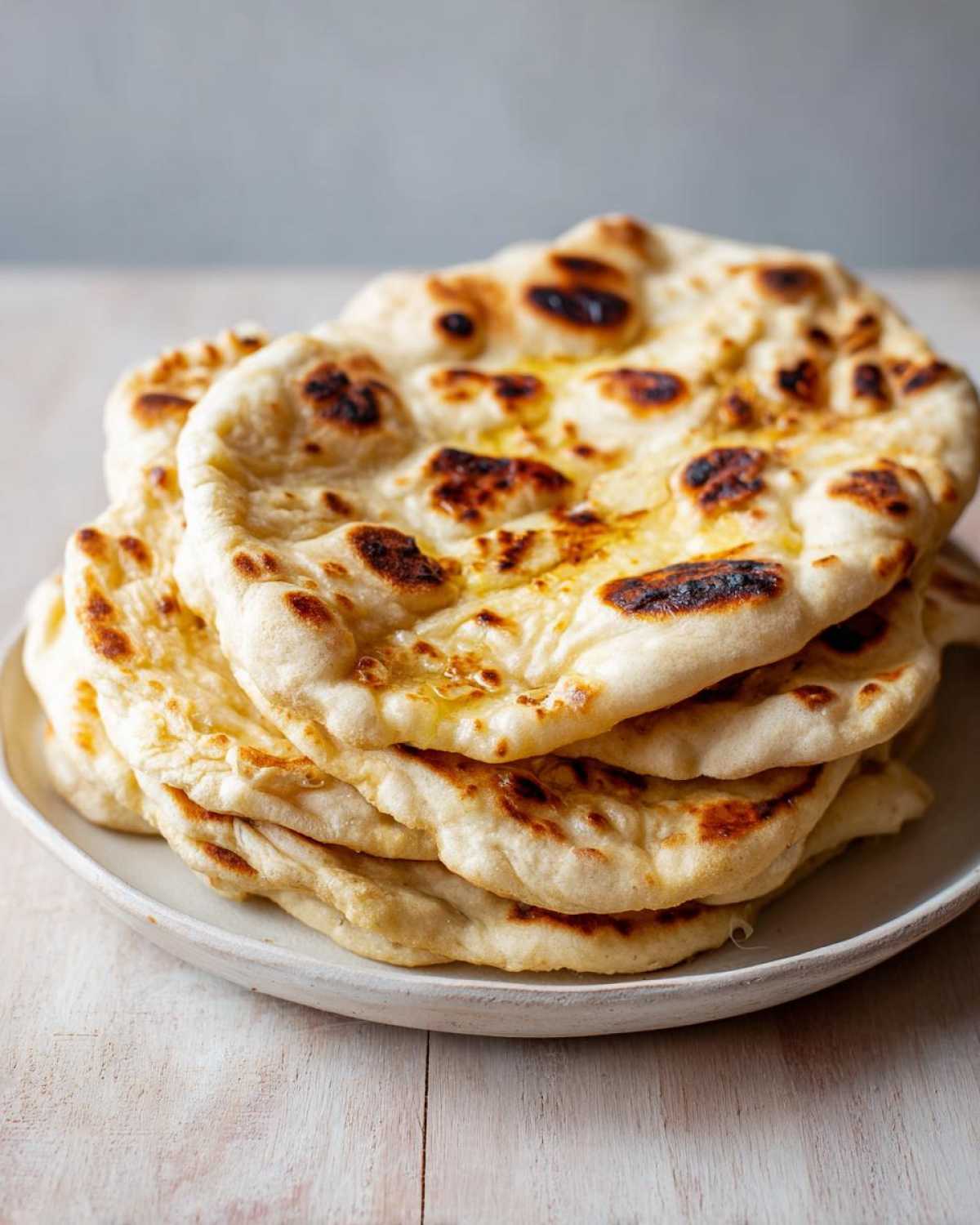 A stack of golden, slightly charred naan bread brushed with butter, ready to serve.