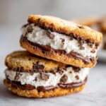 Two stacked cannoli cookies filled with white cream, chocolate drizzle, and mini chocolate chips.