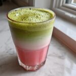 A vibrant, layered strawberry matcha drink showing pink, white, and bright green matcha foam in a glass.