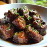 Close-up of rich, dark brown, saucy bites of crockpot steak garnished with fresh chopped parsley.