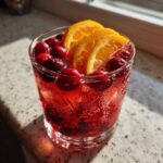 Close-up of a glass filled with bubbling red Thanksgiving punch, garnished with fresh cranberries and orange slices.