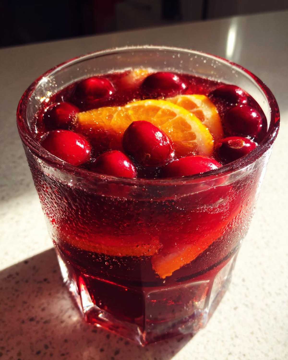 Close-up of a glass filled with sparkling red Thanksgiving punch, garnished with whole cranberries and orange slices.