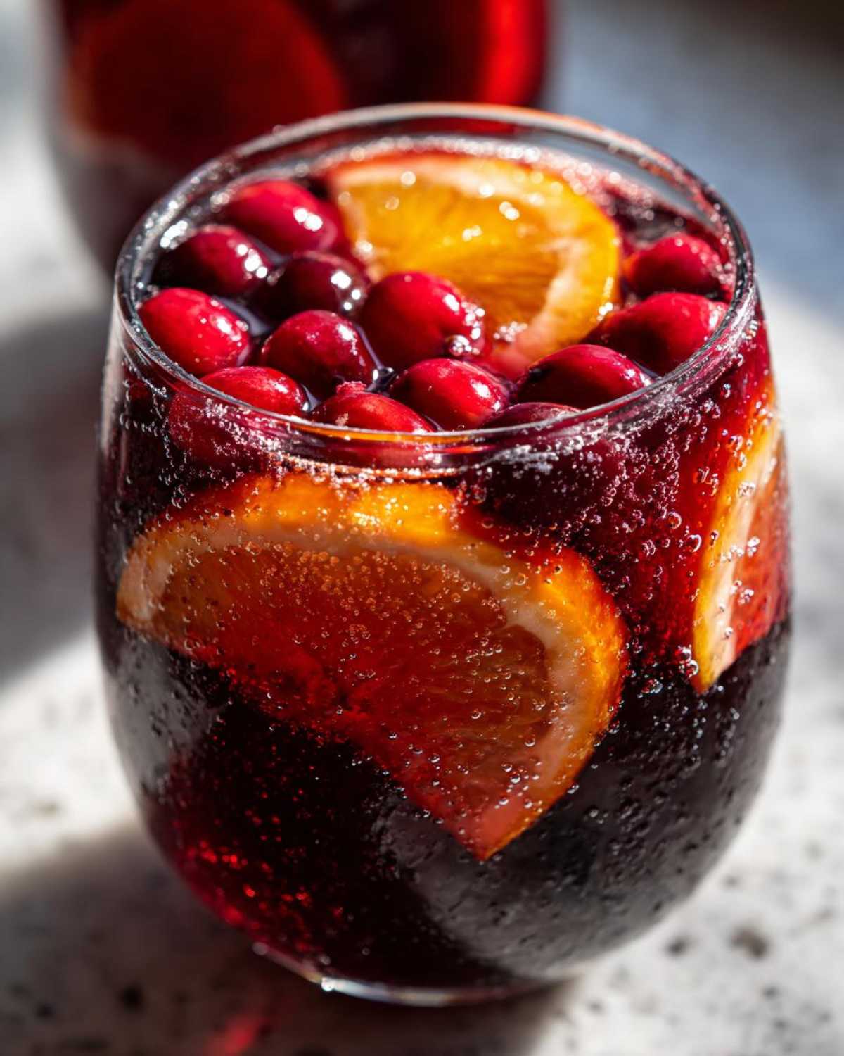 Close-up of a glass filled with sparkling, dark red Thanksgiving punch garnished with fresh cranberries and orange slices.