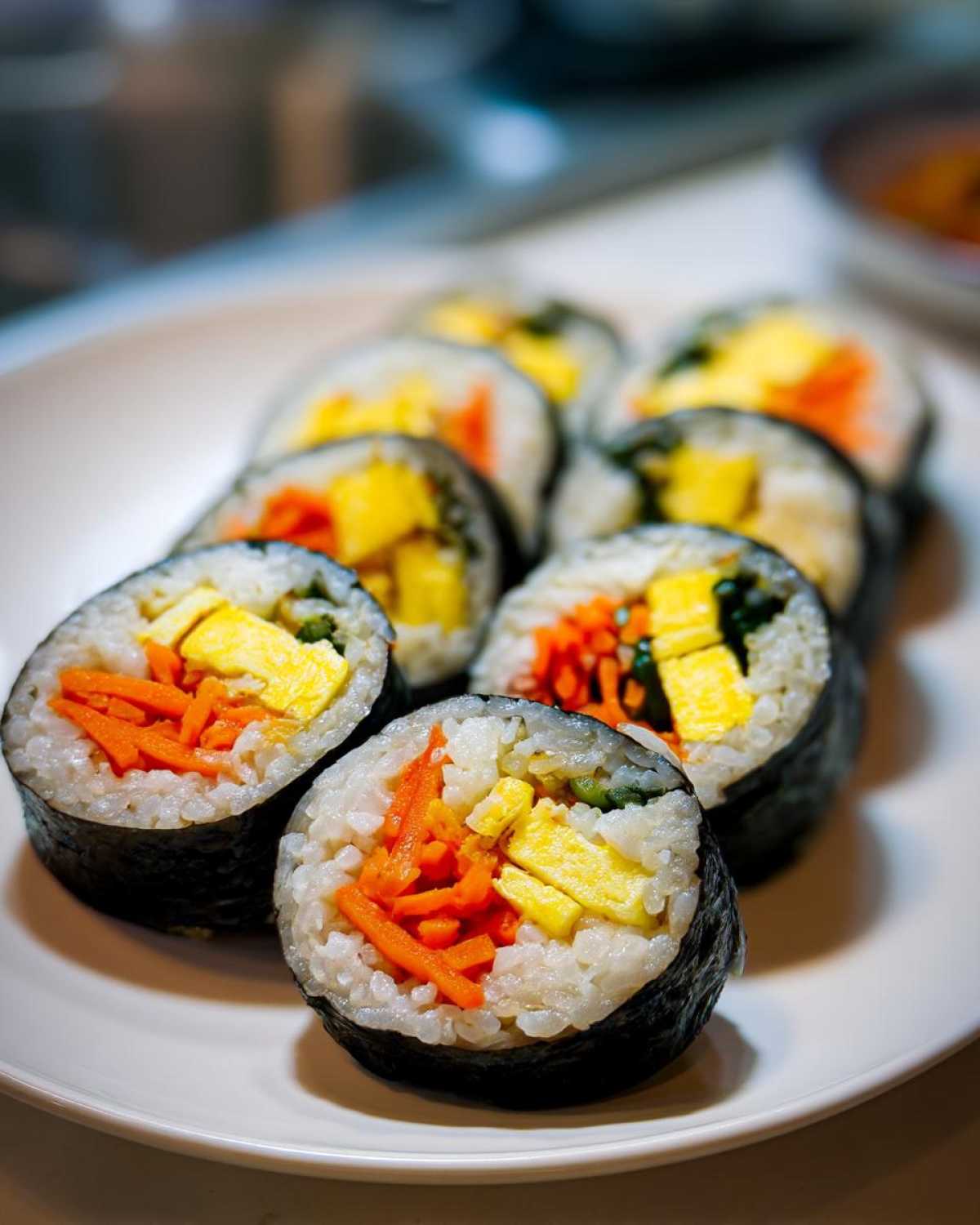 Several slices of homemade tuna kimbap featuring rice, bright orange carrots, and yellow egg on a white plate.