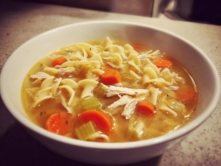 Amazing 1-Hour Turkey Noodle Soup Close-up of a white bowl filled with steaming turkey noodle soup, featuring egg noodles, shredded turkey, carrots, and celery.