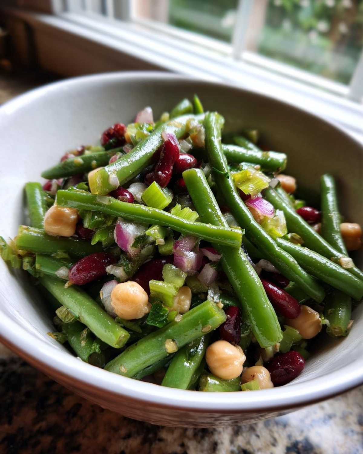 Close-up of a vibrant bean salad featuring green beans, kidney beans, and chickpeas in a white bowl.