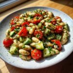 A close-up of a vibrant white bean salad mixed with halved cherry tomatoes, chopped cucumber, and fresh herbs.