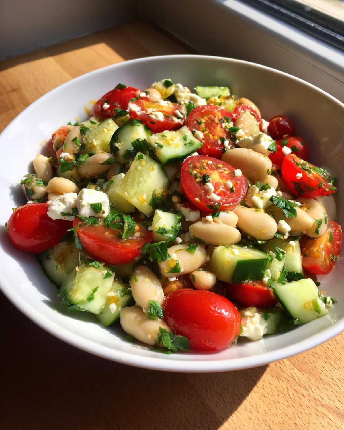 A close-up of a vibrant white bean salad featuring cherry tomatoes, chopped cucumber, feta cheese, and parsley.