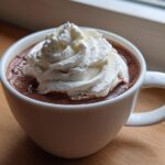 A close-up of rich, dark whipped hot chocolate topped with a generous swirl of white whipped cream.