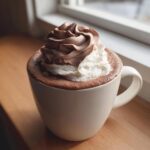 A close-up of rich whipped hot chocolate topped with swirls of chocolate and vanilla whipped cream.
