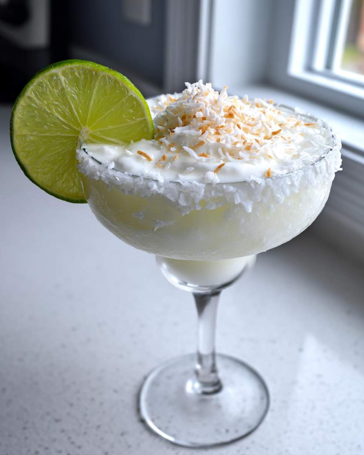 A frosty white Christmas margarita garnished with toasted coconut flakes and a lime wheel.