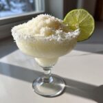 A frozen white christmas margarita topped with shredded coconut and garnished with a lime wheel.