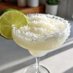 Close-up of a white christmas margarita garnished with a lime slice and a thick rim of shredded coconut.
