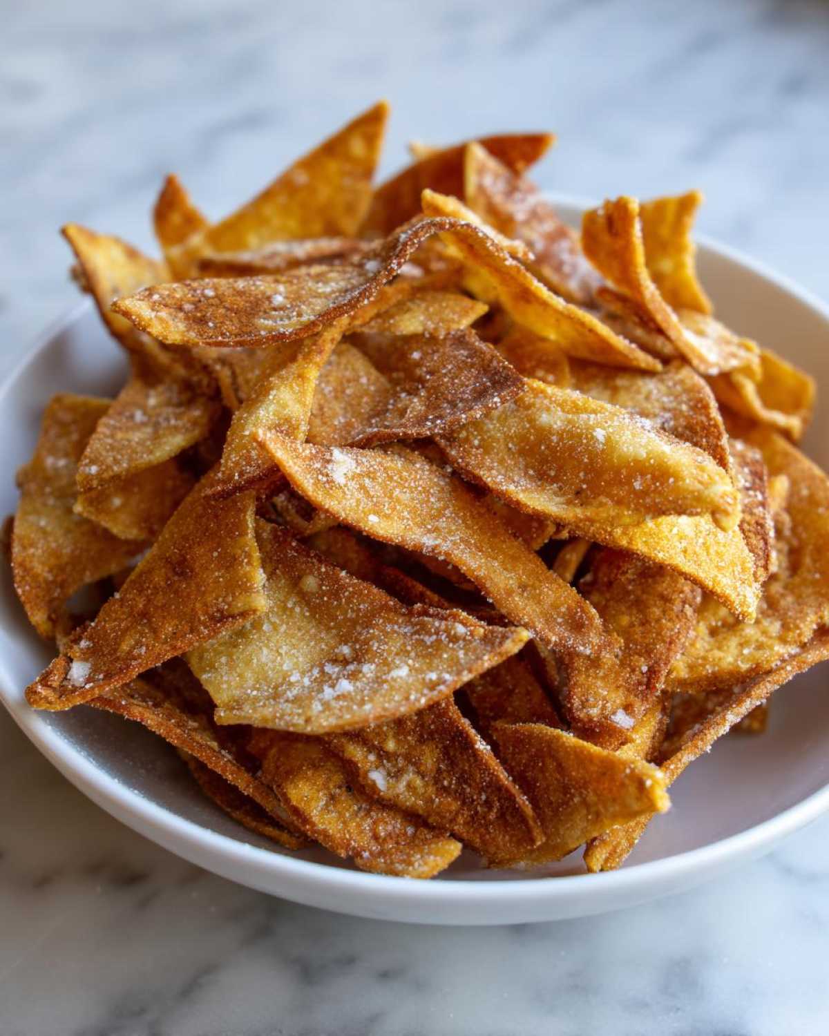 A white bowl filled with golden brown Air Fryer Crispy Tortilla Strips lightly dusted with salt or seasoning.