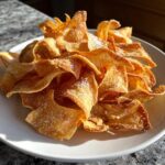 A pile of golden brown Air Fryer Crispy Tortilla Strips lightly dusted with salt, served on a white plate.