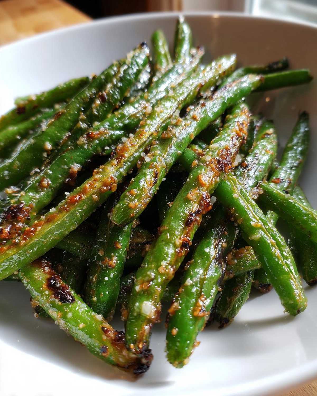 Close-up of vibrant green beans coated in garlic and parmesan seasoning, cooked until slightly charred.