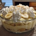 Close-up of layered banana pudding topped with whipped cream swirls and fresh banana slices.