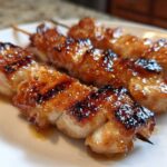 Close-up of three perfectly grilled, glazed chicken skewers with a shiny, caramelized coating.