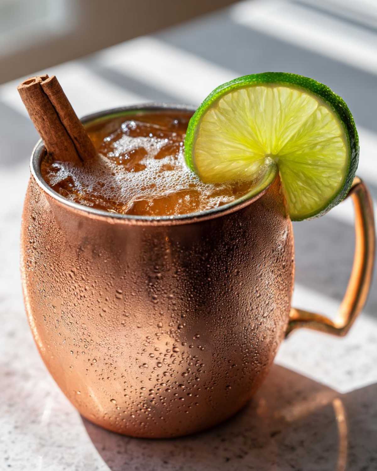 Close-up of a frosty copper mug filled with an apple cider Moscow mule, garnished with a lime wheel and cinnamon stick.