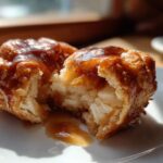 A close-up photo showing a warm apple dumpling broken in half, revealing soft interior and dripping caramel glaze.