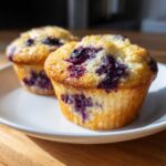Two golden-brown blueberry cottage cheese muffins sitting on a white plate.