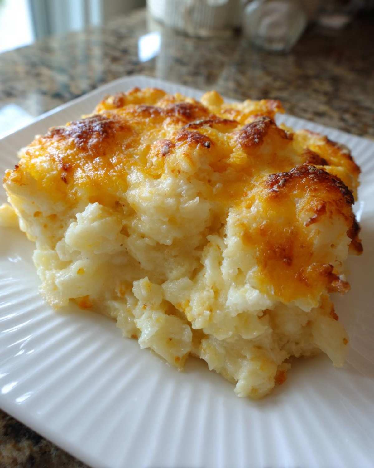A close-up serving of cheesy potato casserole with a golden brown, bubbly cheese topping on a white plate.