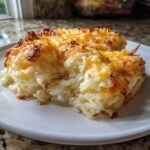 A close-up serving of cheesy potato casserole made with shredded potatoes and a golden, bubbly cheese crust.