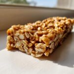 A close-up, side view of a single, chewy no bake granola bar made with oats and a sticky binder, sitting in sunlight.