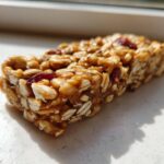 A close-up, sunlit view of a single, chewy no bake granola bar made with oats and dried cranberries.
