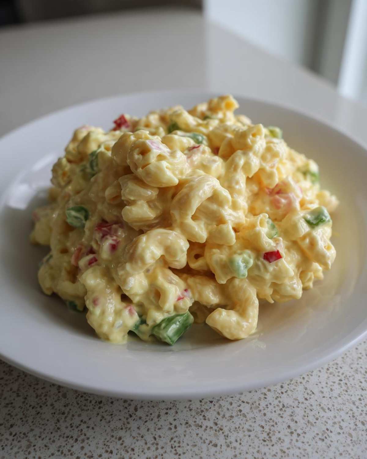 A generous scoop of creamy Copycat Deli-Style Macaroni Salad mixed with chopped red and green peppers, served on a white plate.