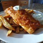 A golden, crispy piece of Copycat Pub-Style Fish and Chips served with thick-cut fries and tartar sauce.