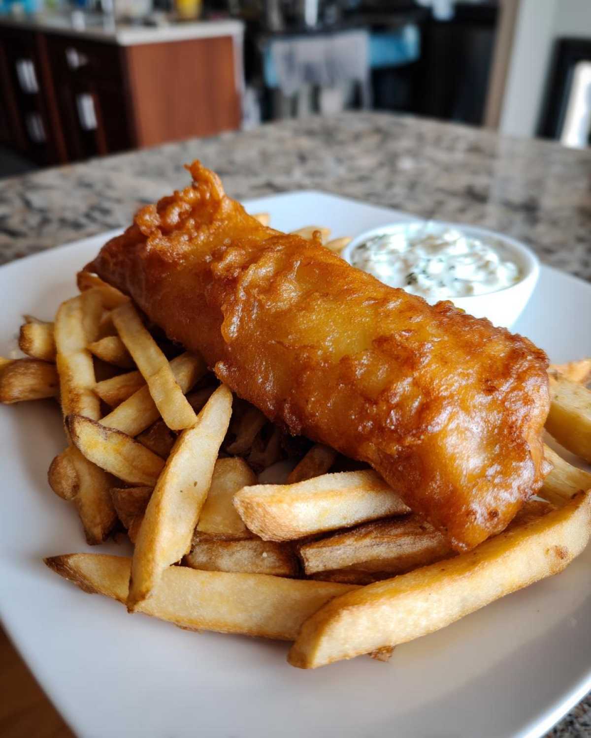 A golden, crispy piece of battered fish served over thick-cut fries with a side of tartar sauce, classic Copycat Pub-Style Fish and Chips.
