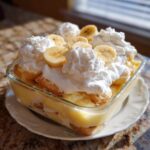 A close-up of homemade banana pudding layered with vanilla wafers, custard, and topped with whipped cream and fresh banana slices.