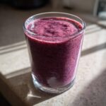 A close-up of a thick, vibrant purple Creamy Blueberry Banana Smoothie served in a clear glass.