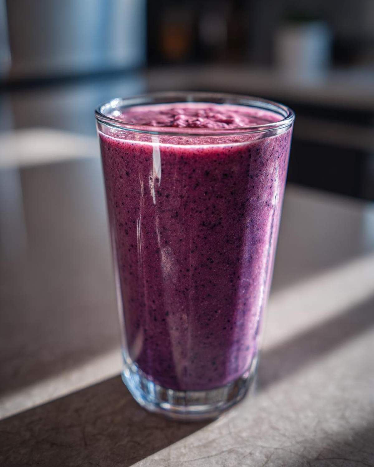 A tall glass filled with a thick, vibrant purple Creamy Blueberry Banana Smoothie, sitting on a countertop.