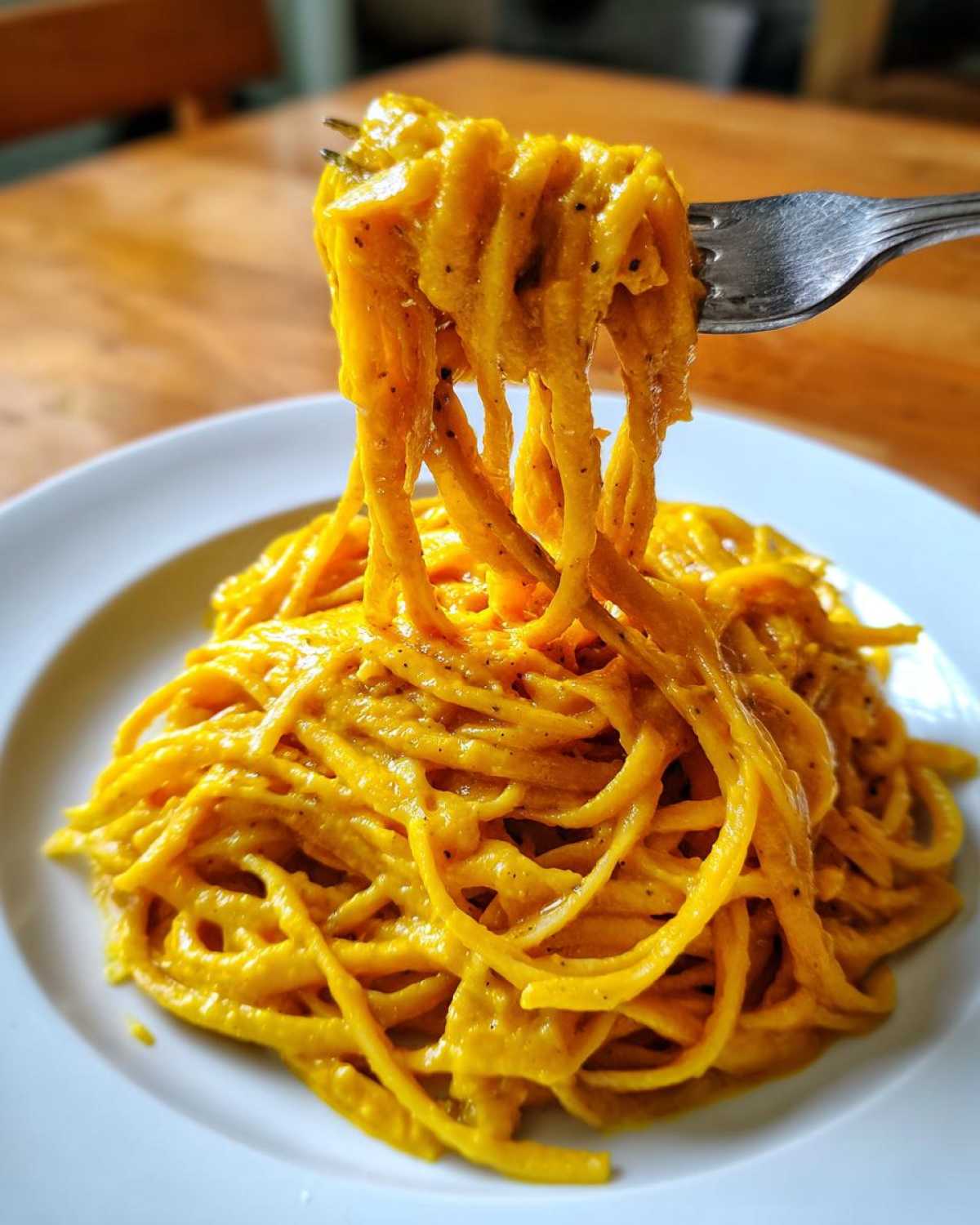 A fork lifts strands of spaghetti coated in a thick, vibrant orange butternut squash pasta sauce.
